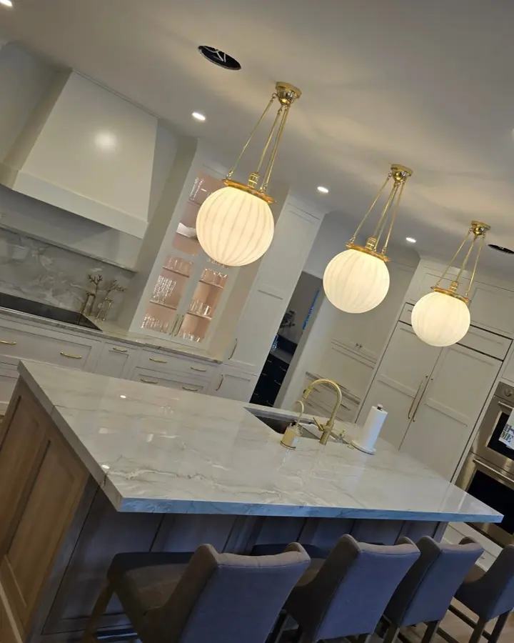 Quartzite island under three globe pendant lights in a white kitchen