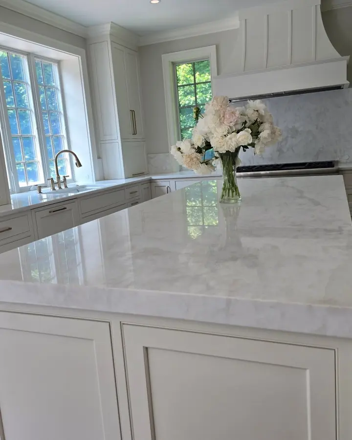 White kitchen island in Calacatta Zambia marble with a vase of white flowers