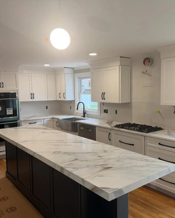 White kitchen with a gray-veined island and dark appliances