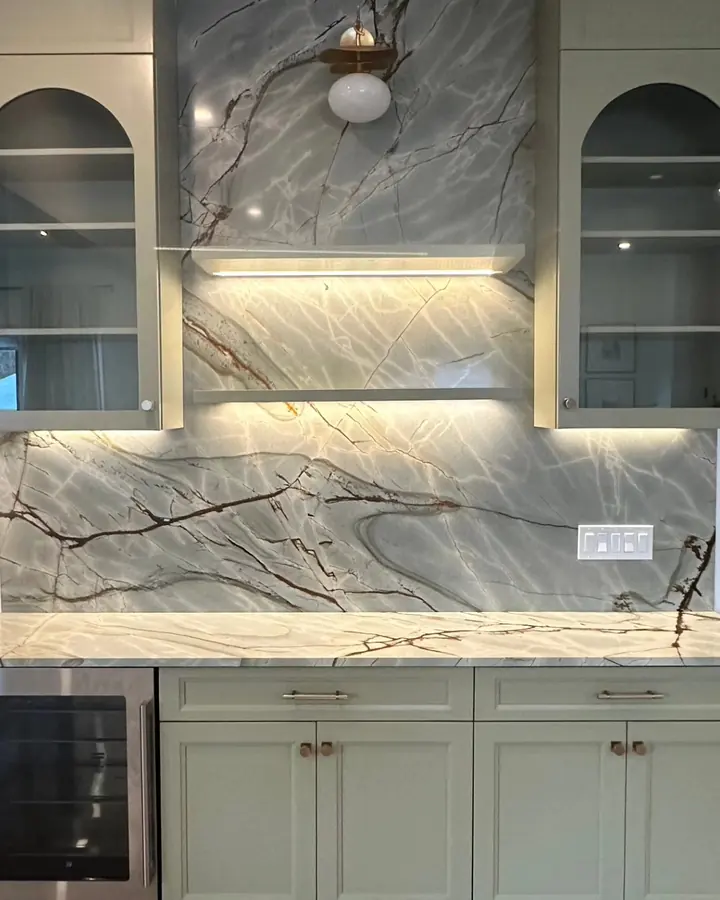 Wet bar with sage cabinets, glass doors and a full-height slab backsplash with dark veins